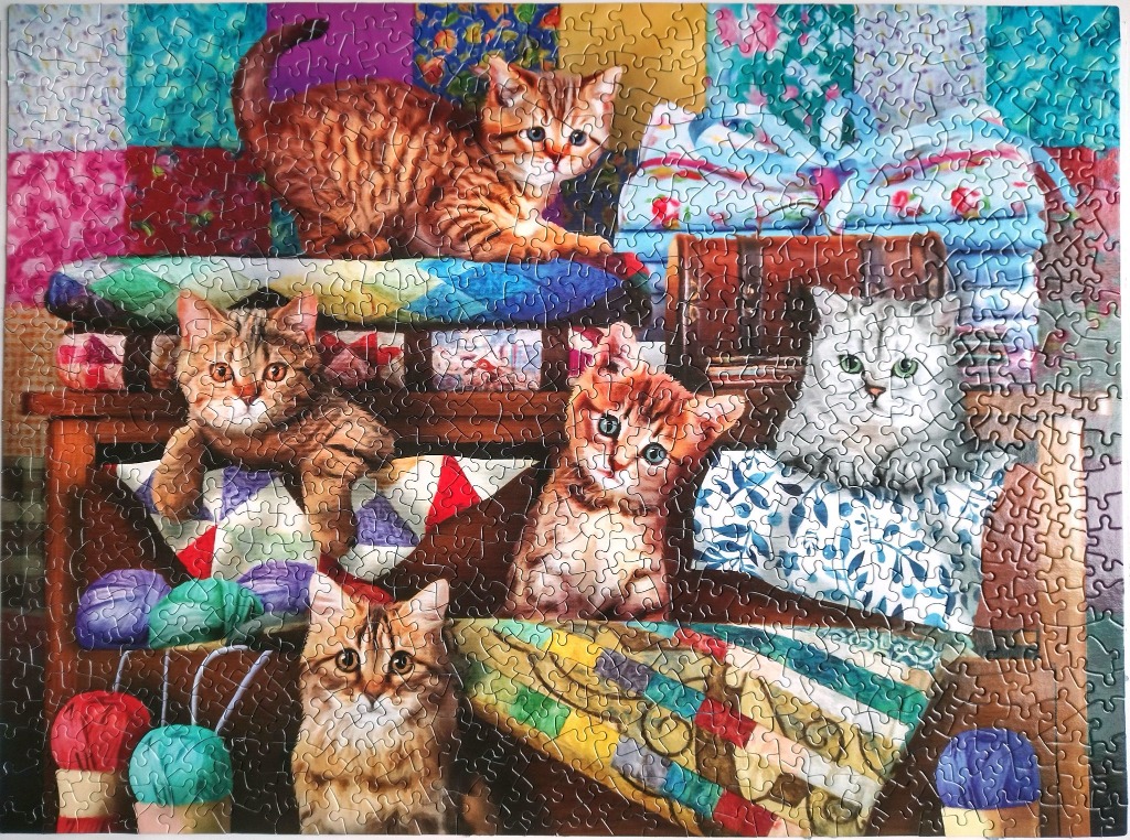 A cozy scene of four kittens sitting among colorful fabric quilts and yarn.