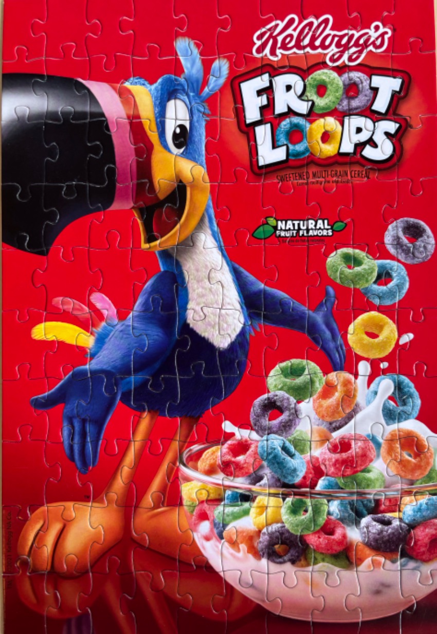 Toucan Sam mascot next to a bowl of colorful fruit-shaped cereal against a bright red background.