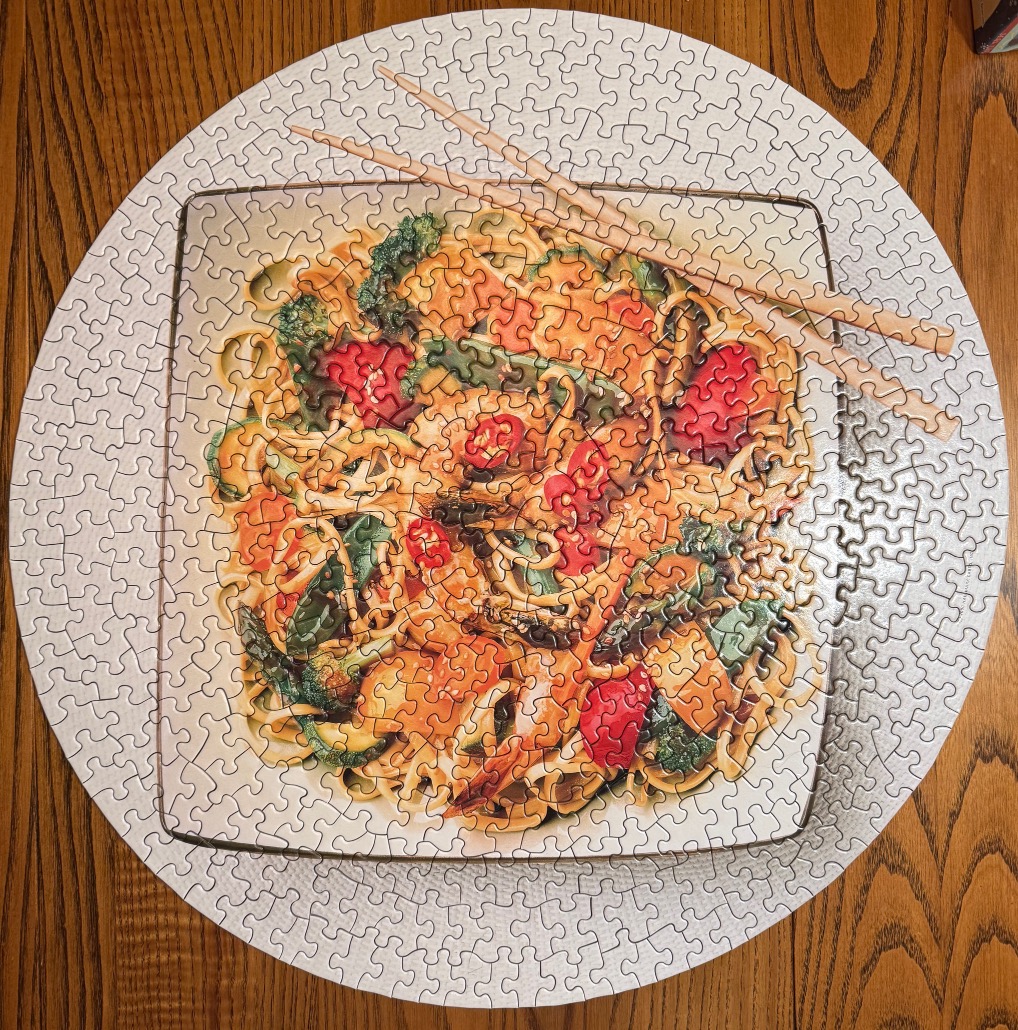 A top-down view of a square plate of colorful stir-fried noodles with chopsticks resting on top, set on a round background.