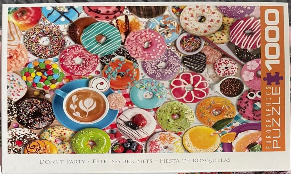 A top-down view of a spread of various colourful donuts, a coffee cup, and fruit arranged on a checkered tablecloth.