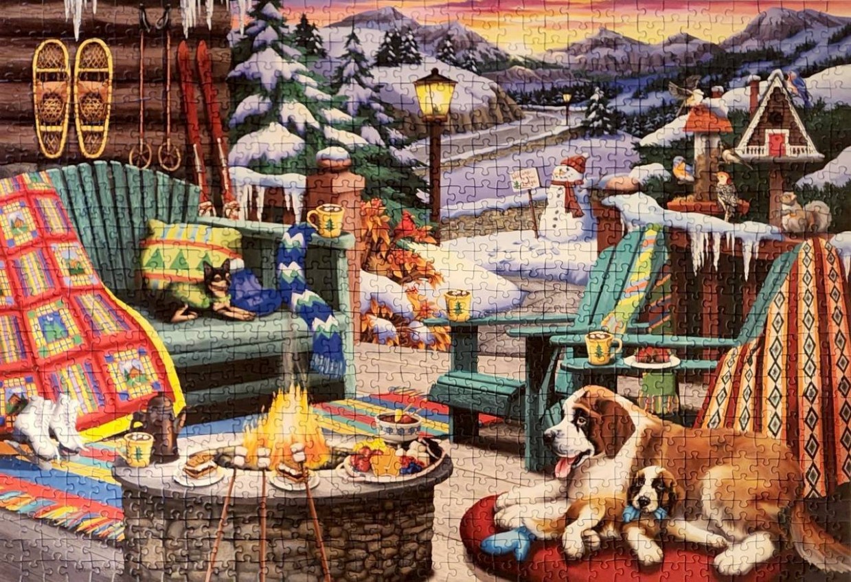 A cozy winter patio scene with a fire pit, two dogs, and a snow-covered mountain landscape at sunset.