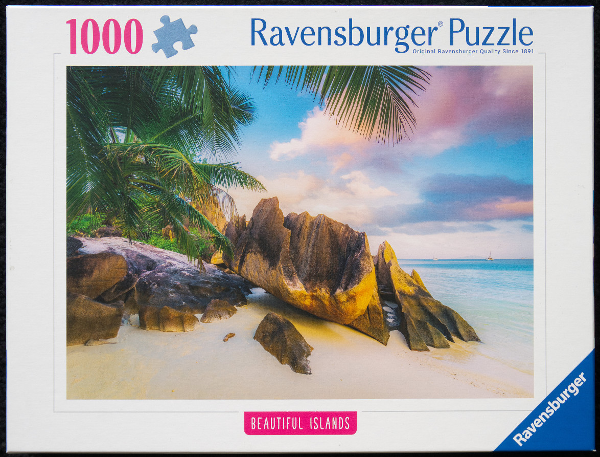 A tropical beach scene with large granite boulders, white sand, and palm trees under a sunset sky.