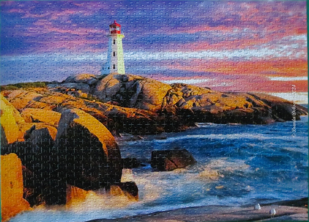 A scenic photograph of a white lighthouse on a rocky coast at sunset with vibrant orange and purple clouds.