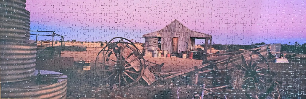 A panoramic photograph of a rustic, corrugated iron outbuilding in the Australian outback at sunset.
