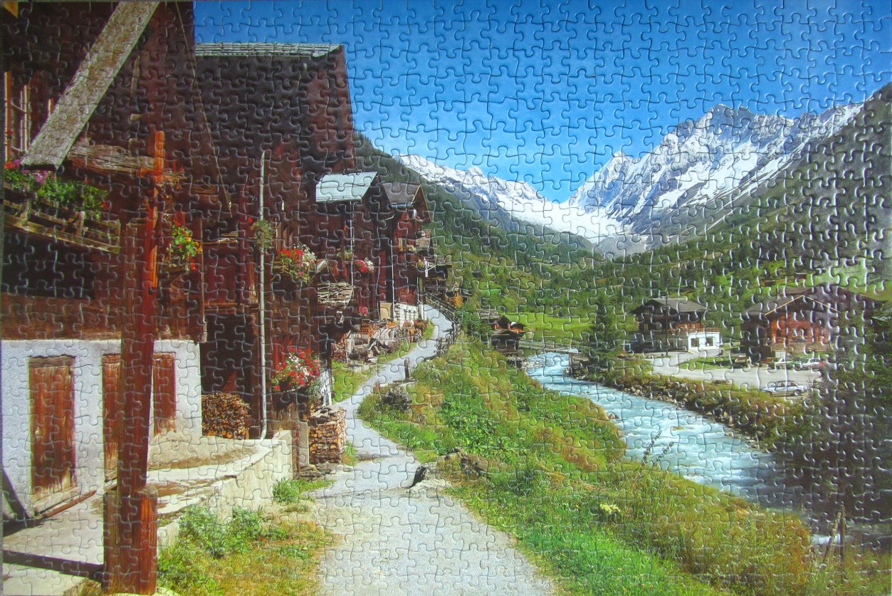 A charming Swiss-style village nestled in a sunny valley with snow-capped mountains in the background.