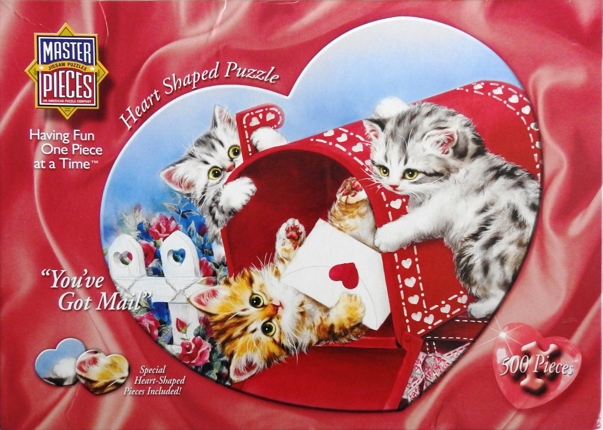 Three kittens playing with a red mailbox shaped like a heart, surrounded by flowers and white picket fencing.
