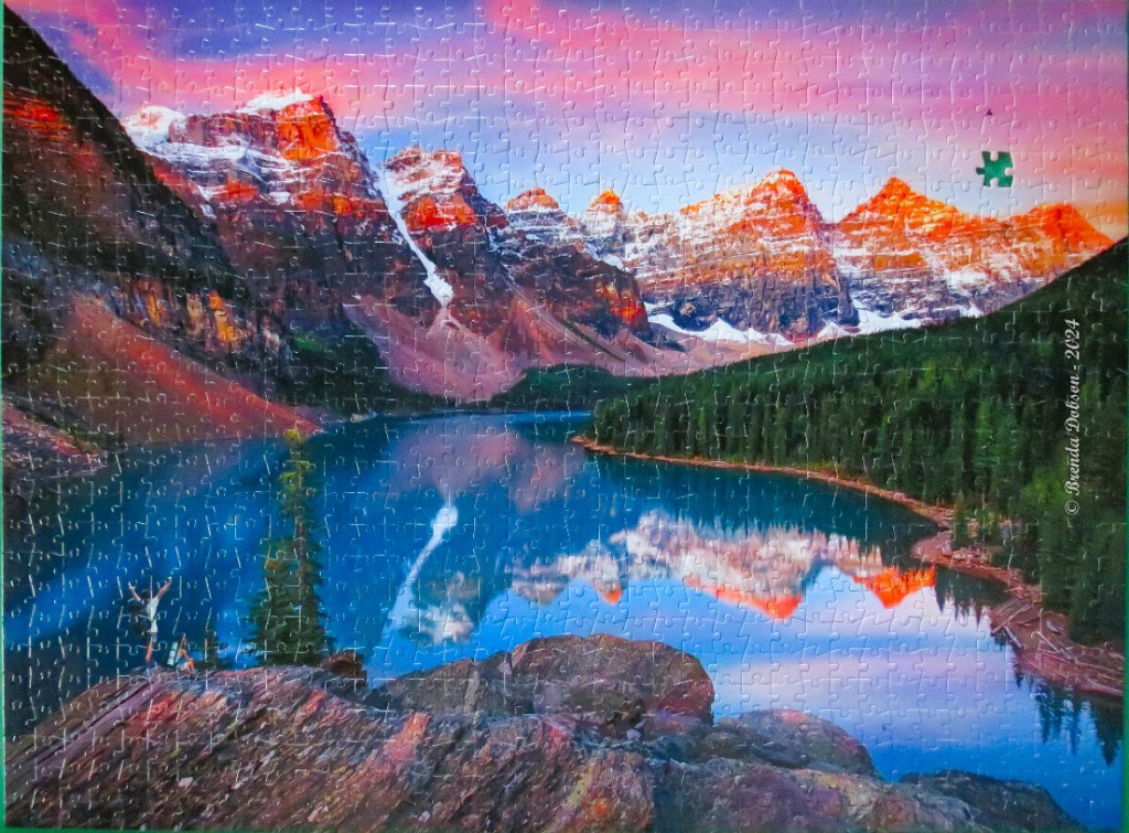A panoramic landscape of Moraine Lake at sunrise with snow-capped peaks reflecting in the deep blue water.