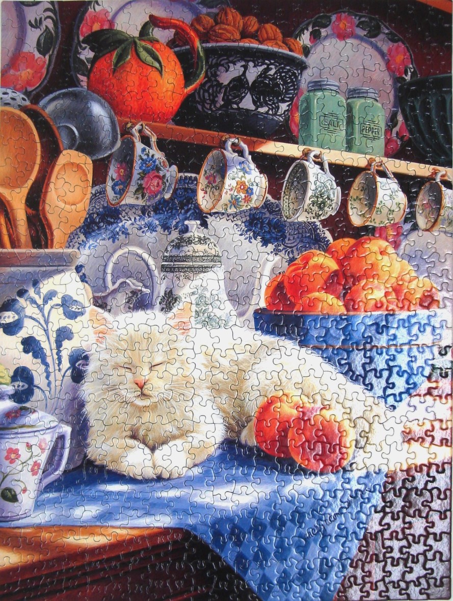 A fluffy white cat sleeping peacefully on a blue tablecloth in a kitchen filled with pottery and fruit.