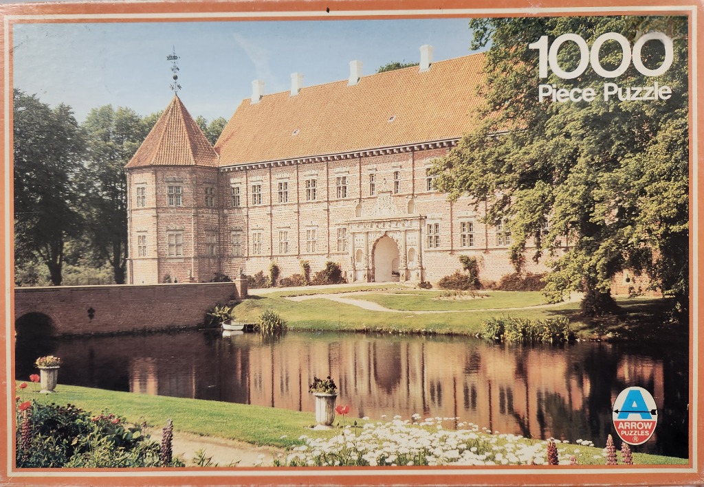 A stately brick manor house with a tall turret reflecting in a calm moat surrounded by trees and flowers.