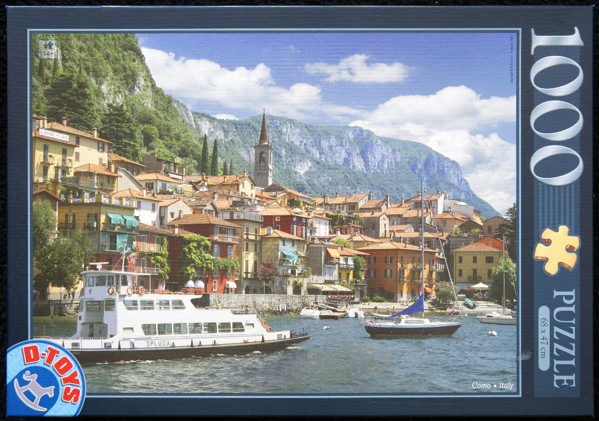 Scenic view of Varenna, Lake Como, Italy, with a ferry, sailboats, and colorful village houses against mountains.
