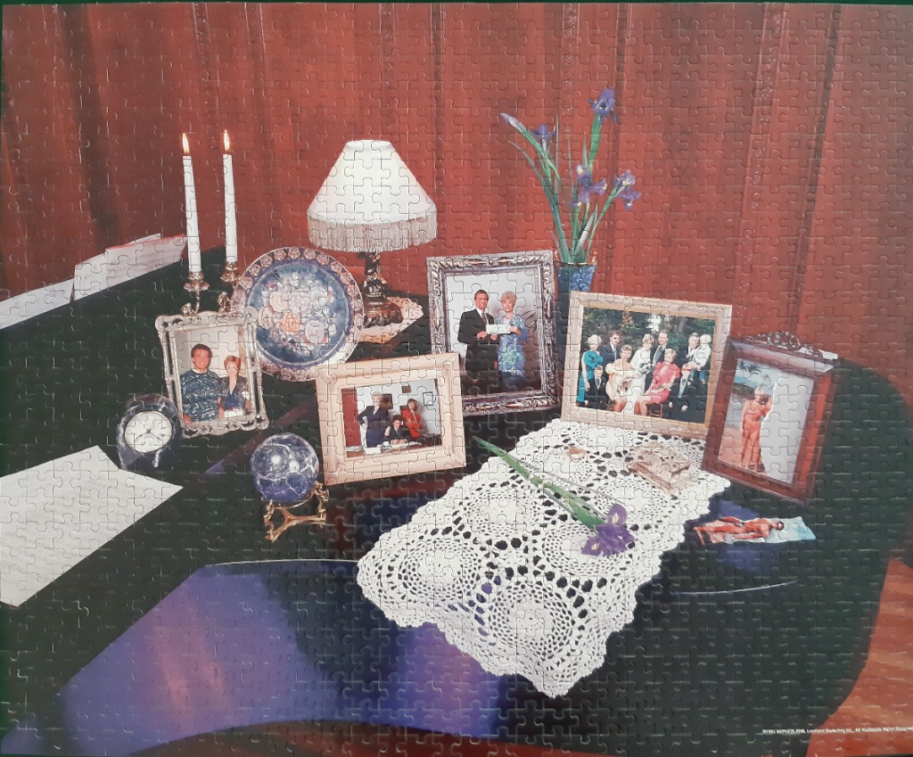 A formal collection of framed family portraits, candles, and a lamp on a dark, polished surface.
