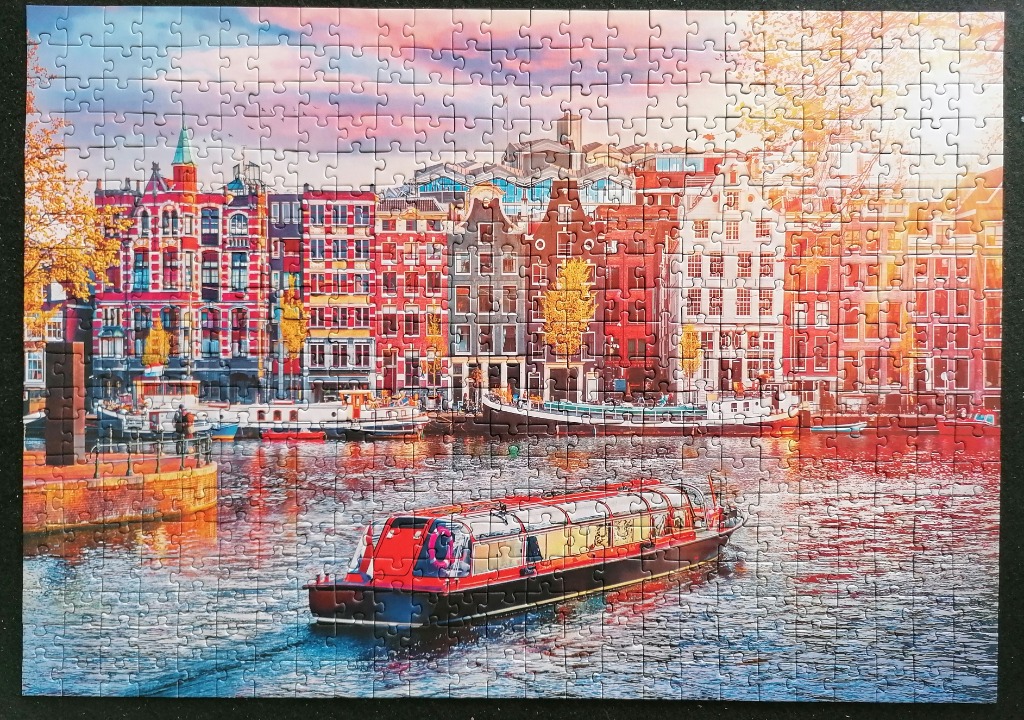 A canal scene in Amsterdam with traditional townhouses and a red tour boat at sunset.