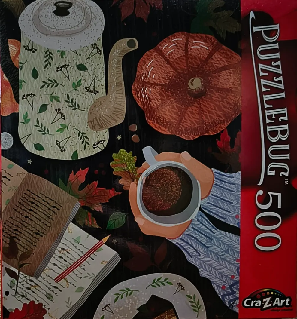 Autumn themed still life with a teapot, pumpkin, book, and a person holding a mug of warm drink.