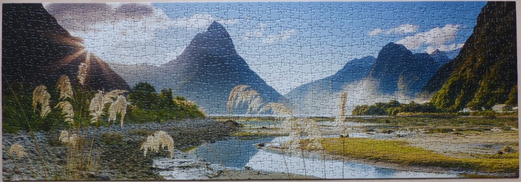 A panoramic landscape featuring Mitre Peak in Milford Sound, New Zealand, with tall grasses in the foreground.