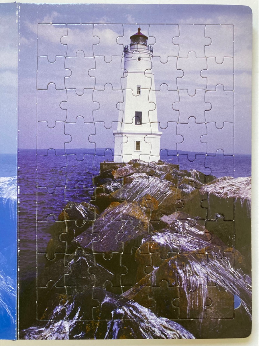A white lighthouse standing at the end of a rocky breakwater over dark blue water.