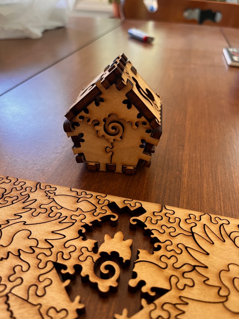 Wooden laser-cut 3D house puzzle, with intricate scrollwork and leaf patterns.