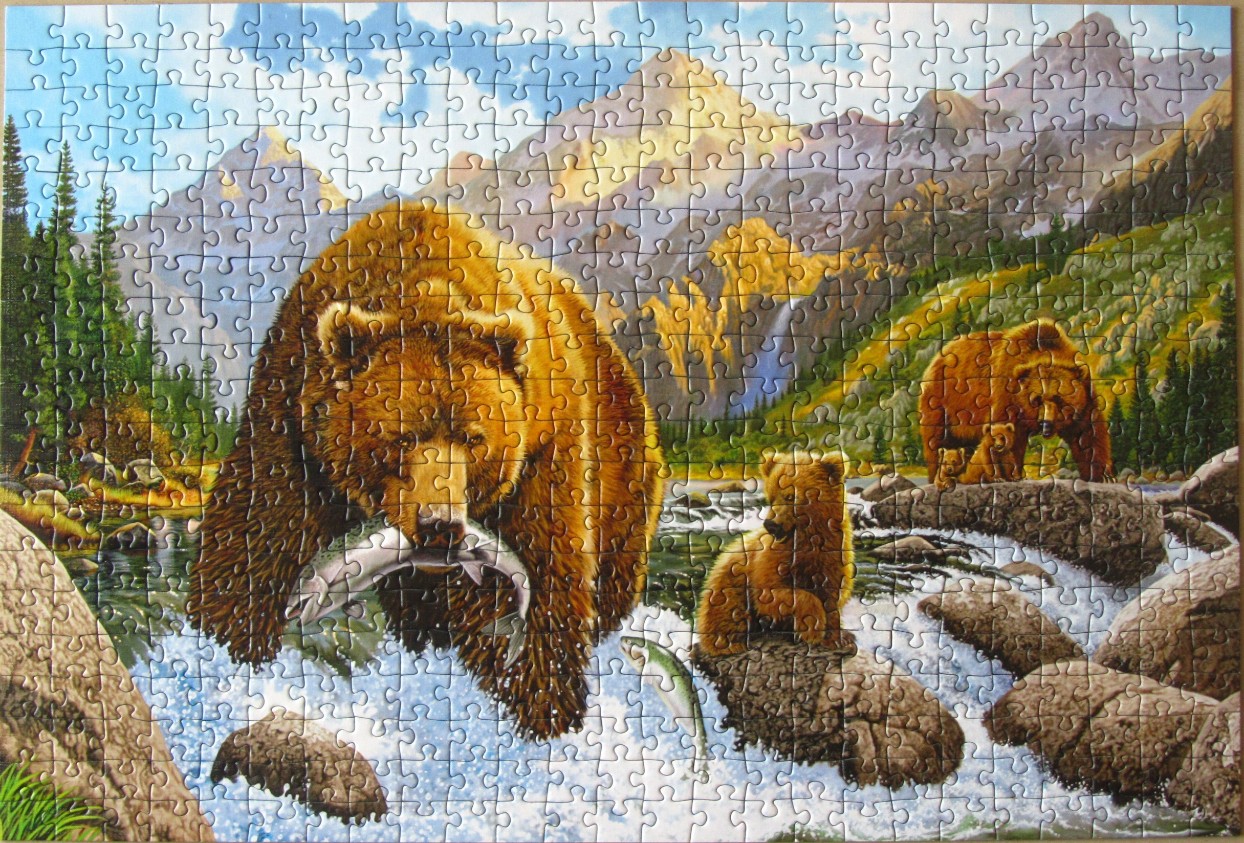 A grizzly bear with a fish in its mouth and two cubs near a river in a mountain landscape.