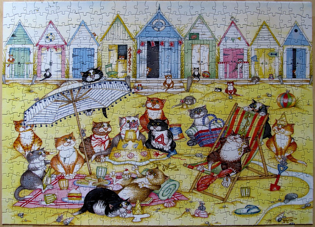 A whimsical illustration of many cats playing on a sandy beach in front of a row of colorful beach huts.