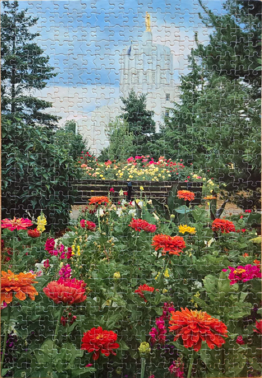 A view of the Portland Oregon Temple framed by lush green trees and a vibrant foreground of orange and red flowers.