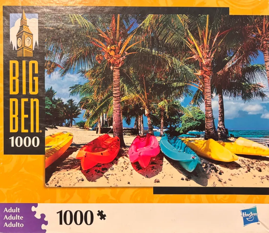 A row of colorful kayaks parked on a sandy beach under tall tropical palm trees by the ocean.