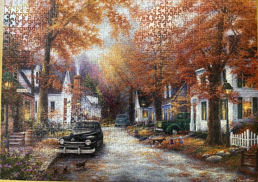 A nostalgic autumn street scene with classic cars, white houses, and vibrant fall foliage.