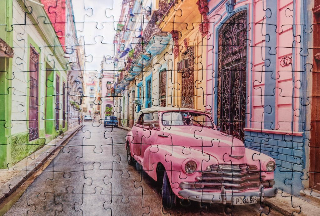 A vintage pink convertible car parked on a narrow, colorful street in Havana, Cuba.