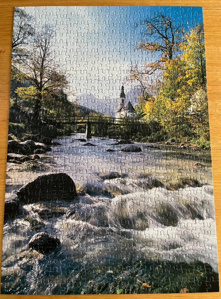 A peaceful landscape featuring a church across a river with autumn trees and mountains in the background.