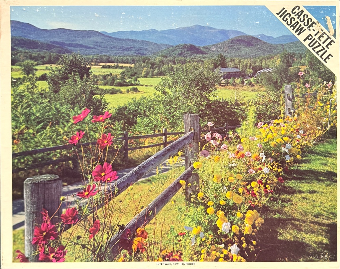 A rural New Hampshire landscape featuring a vibrant flower garden in the foreground and distant rolling mountains.