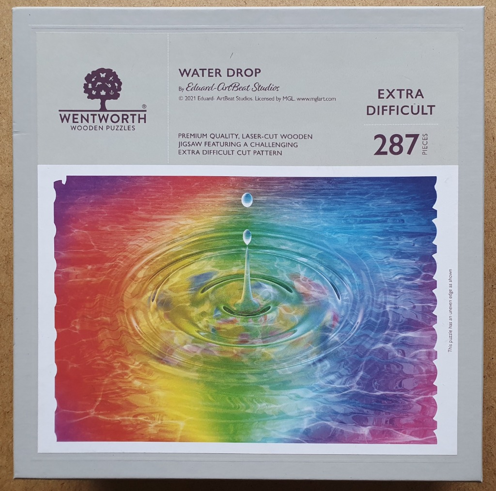 Close up of a water droplet falling into a vibrant rainbow-colored liquid surface, creating concentric ripples.