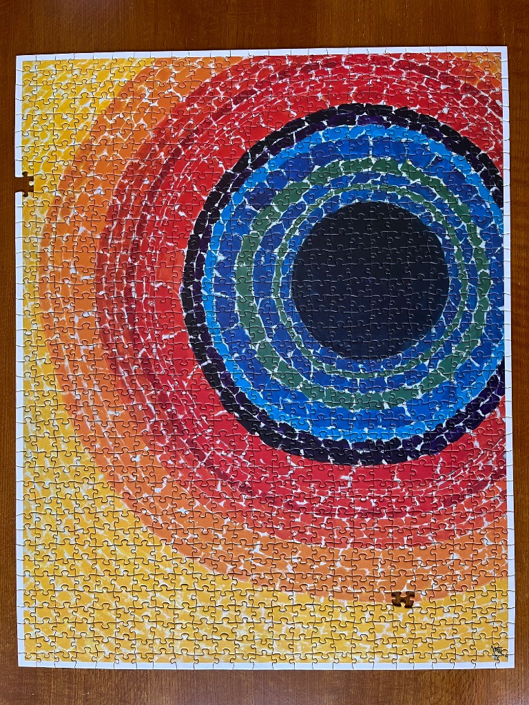 An abstract painting of concentric circles radiating from a black center, with a vibrant color palette of yellow to red.