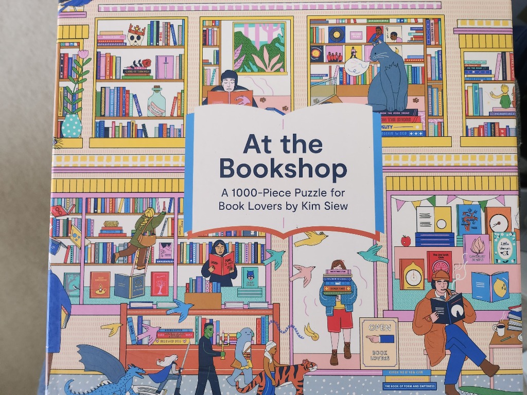 A colorful, detailed illustration of a two-story bookshop filled with diverse characters reading and browsing shelves.