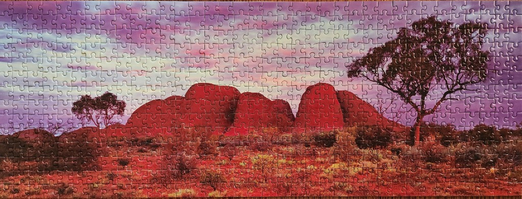 Panoramic view of Uluru at sunset with surrounding outback landscape and trees.