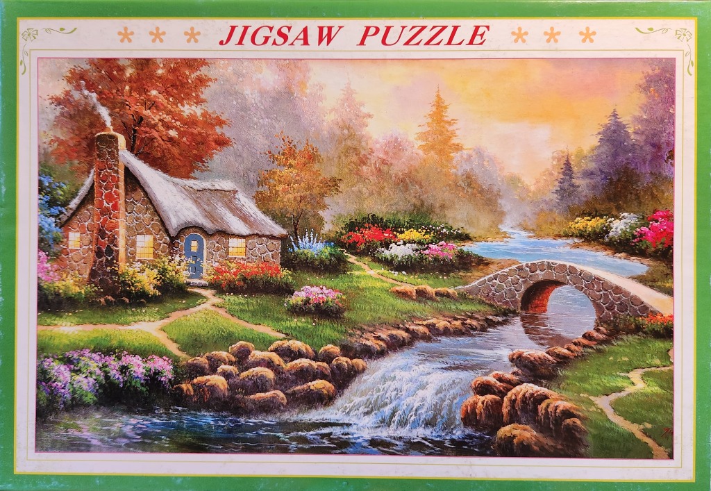 A cozy stone cottage with a thatched roof sits beside a meandering stream and a stone arch bridge at sunset.