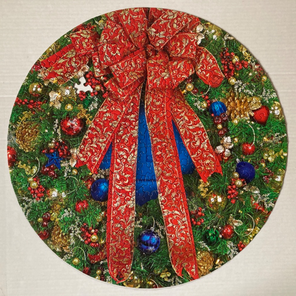 A circular Christmas wreath decorated with ornaments and a large red and gold patterned ribbon.