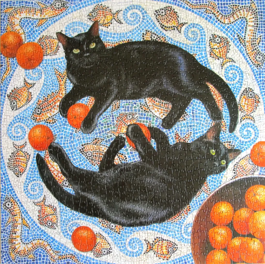 Two black cats lounging on a blue mosaic tile surface decorated with orange fruit and fish patterns.