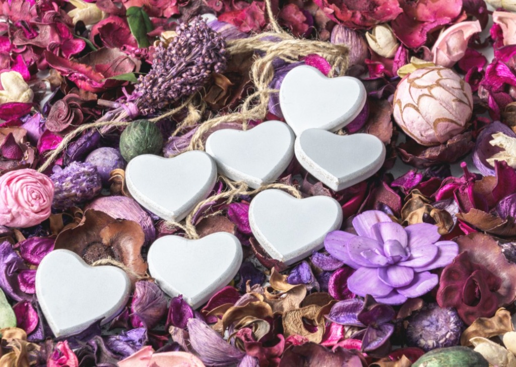 Six white heart ornaments nestled in a bed of purple and pink potpourri