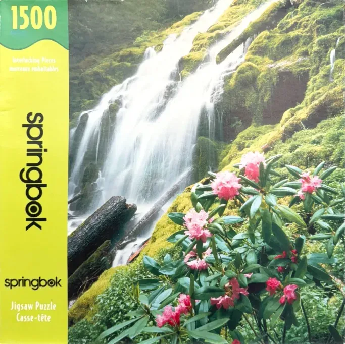 A lush waterfall cascading over mossy rocks with a foreground of pink rhododendron flowers.