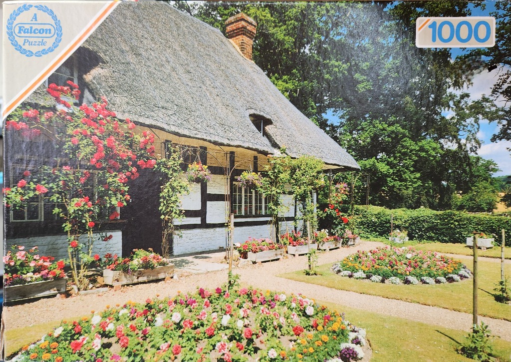 A traditional English cottage with a thatched roof, black timber framing, and a vibrant garden filled with red roses.
