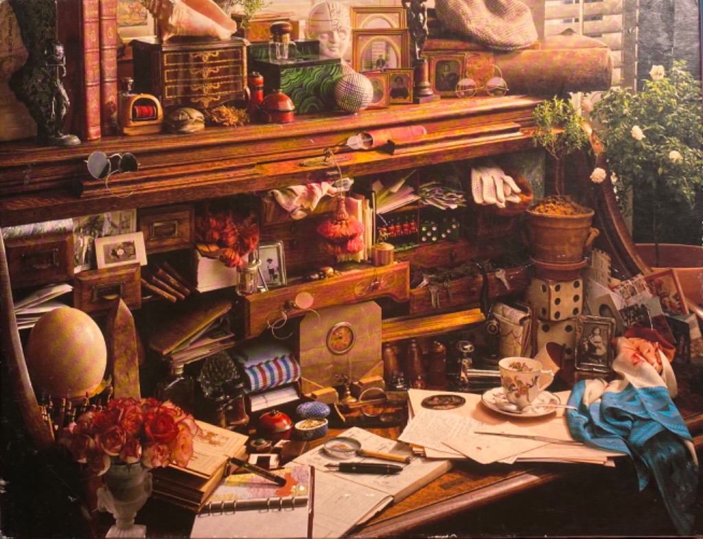 A cluttered antique roll-top desk filled with books, trinkets, stationery, and flowers in a warm, nostalgic setting.