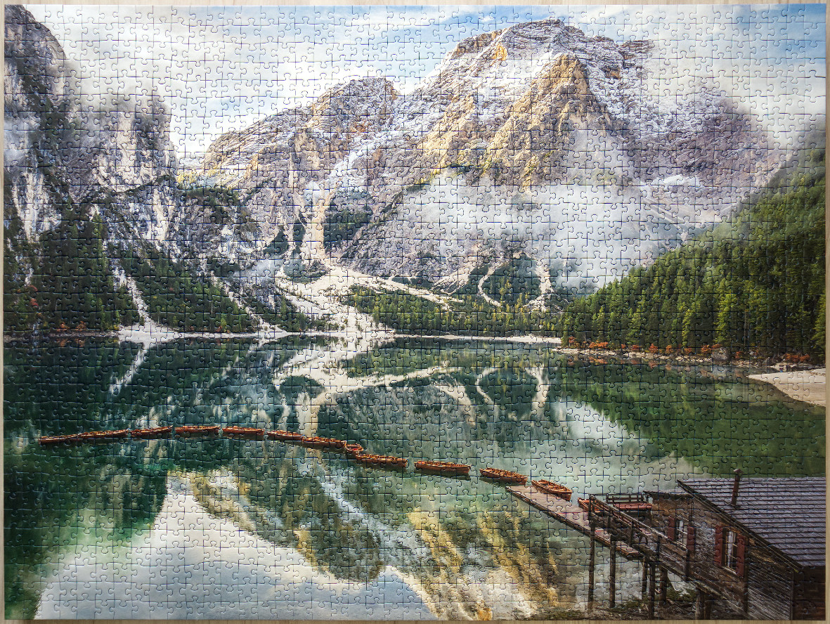 A row of wooden rowboats tethered to a wooden pier on a calm lake beneath towering, snow-dusted dolomite mountains.