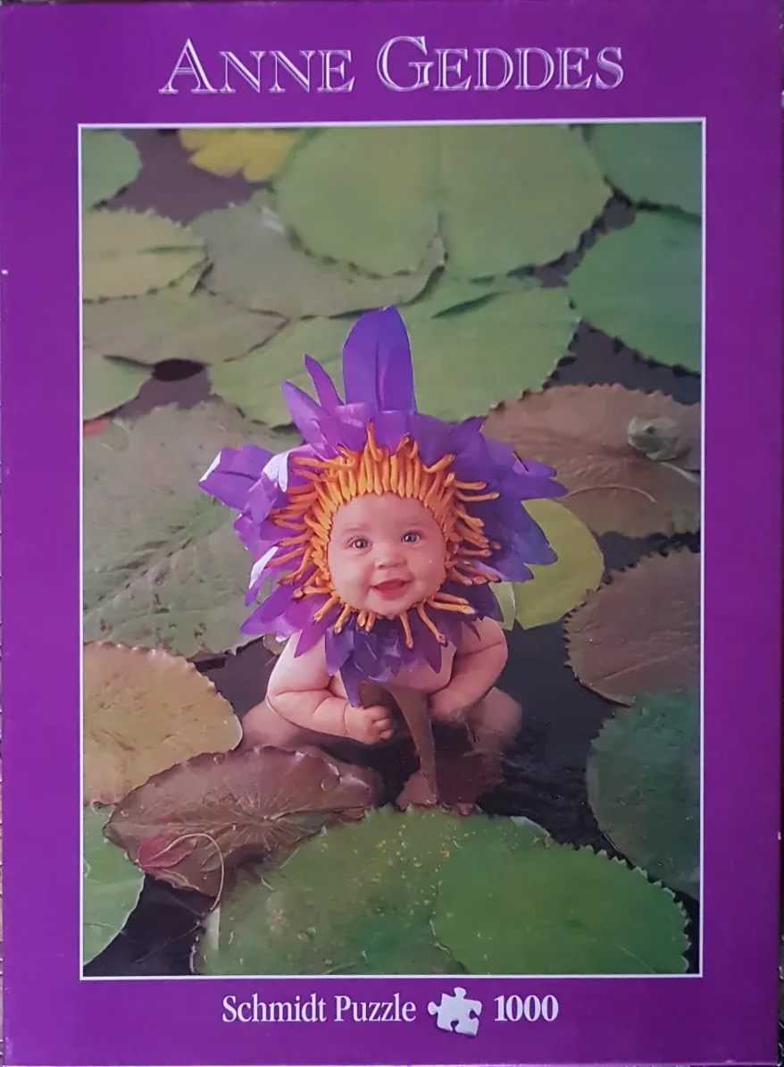 A baby dressed as a purple water lily flower sits among lily pads in a pond.