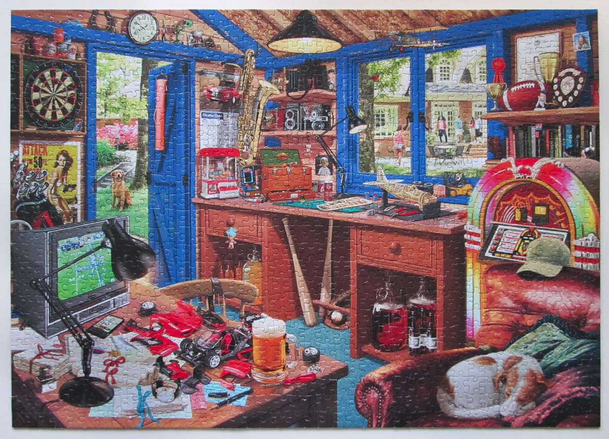 A cluttered man cave or hobby room filled with toys, tools, a jukebox, and a dog sleeping on a chair.