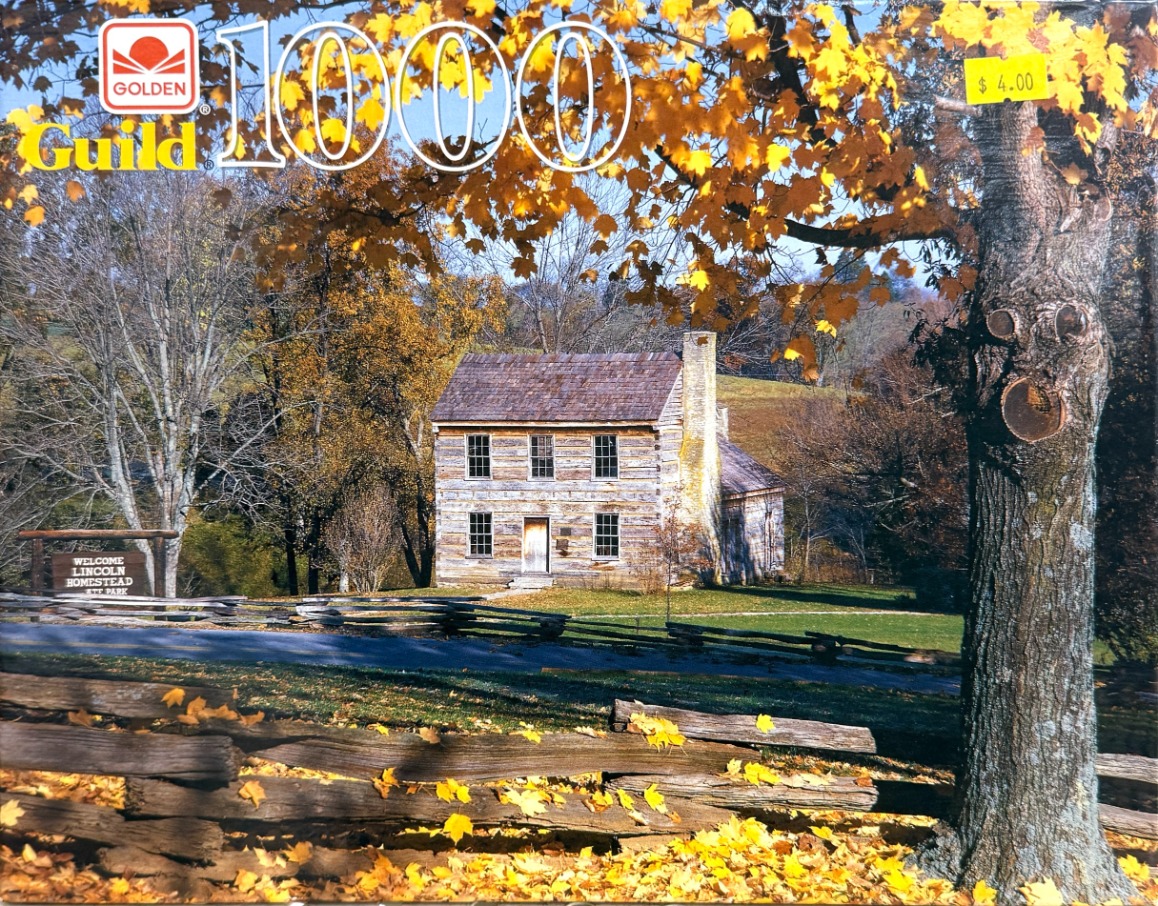 A rustic two-story log cabin surrounded by autumn trees and a wooden fence.