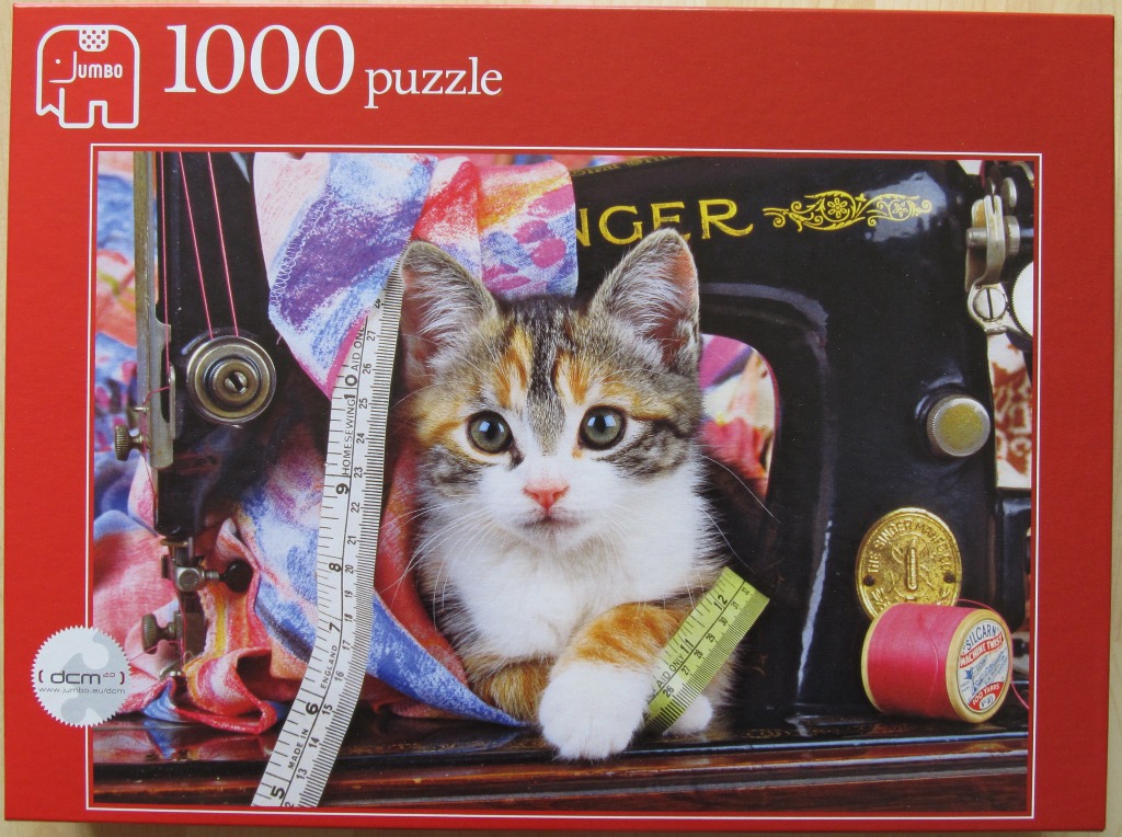 A calico kitten peeking through an antique sewing machine surrounded by fabric and sewing supplies.
