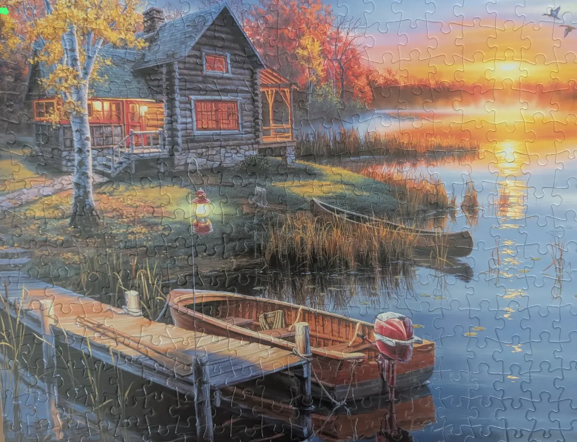 A cozy log cabin beside a lake at sunset with a wooden dock and a small boat in the foreground.