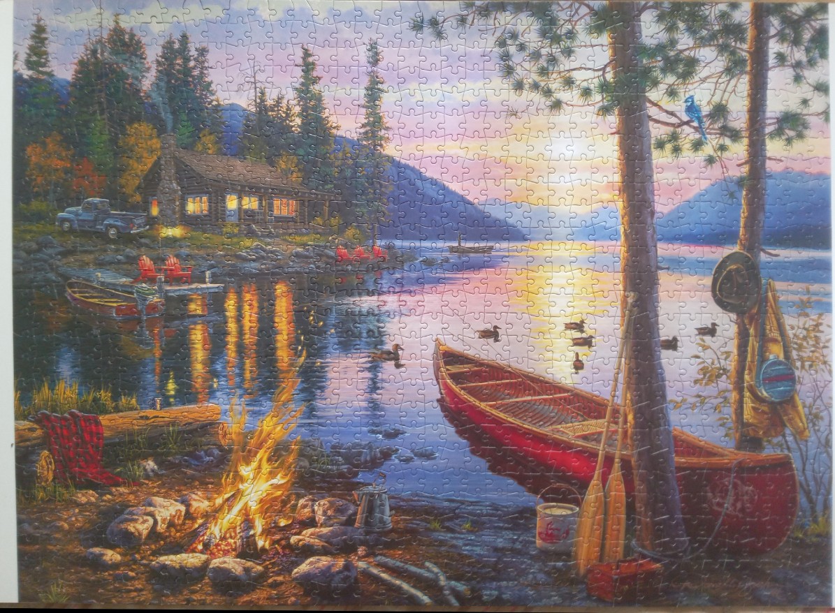 A peaceful lakeside cabin scene at sunset with a campfire, a red canoe, and a view of distant mountains.
