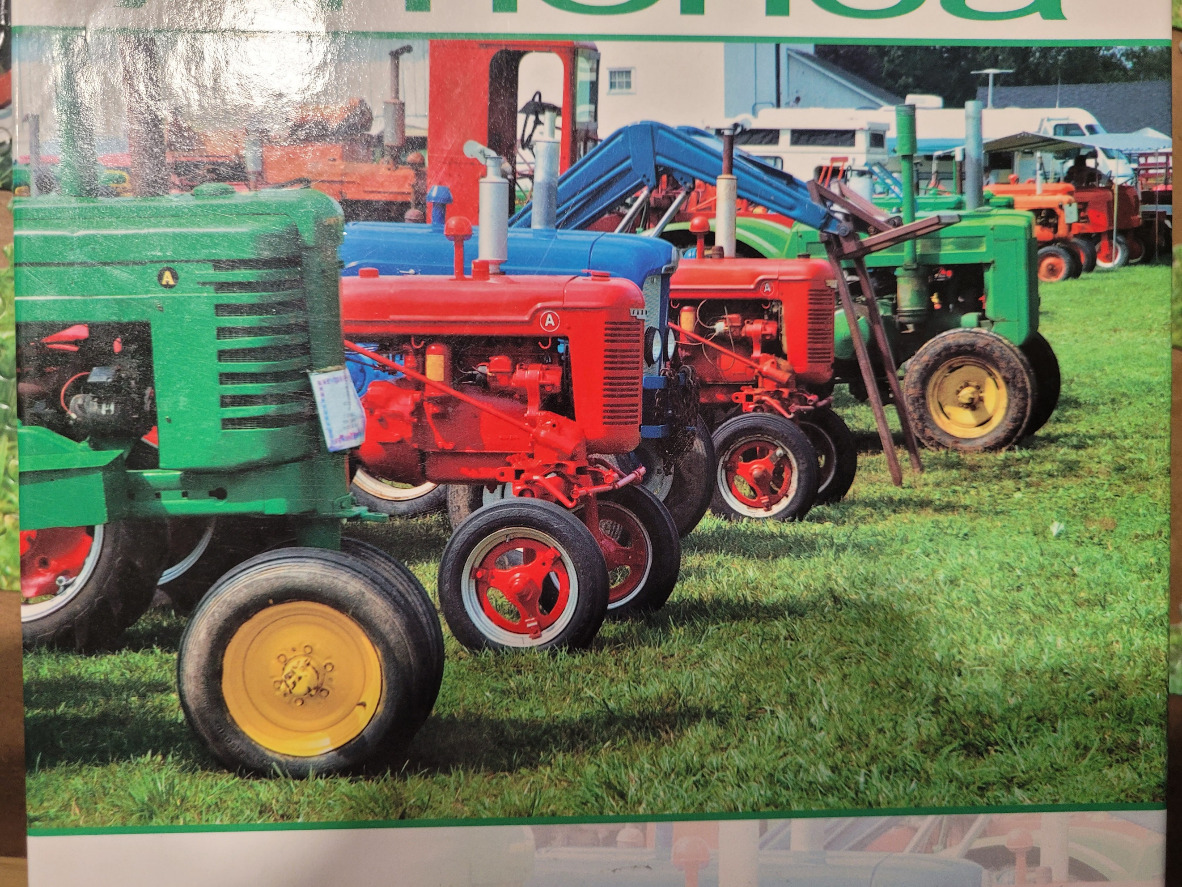 A row of colorful vintage farm tractors parked on a grassy field.