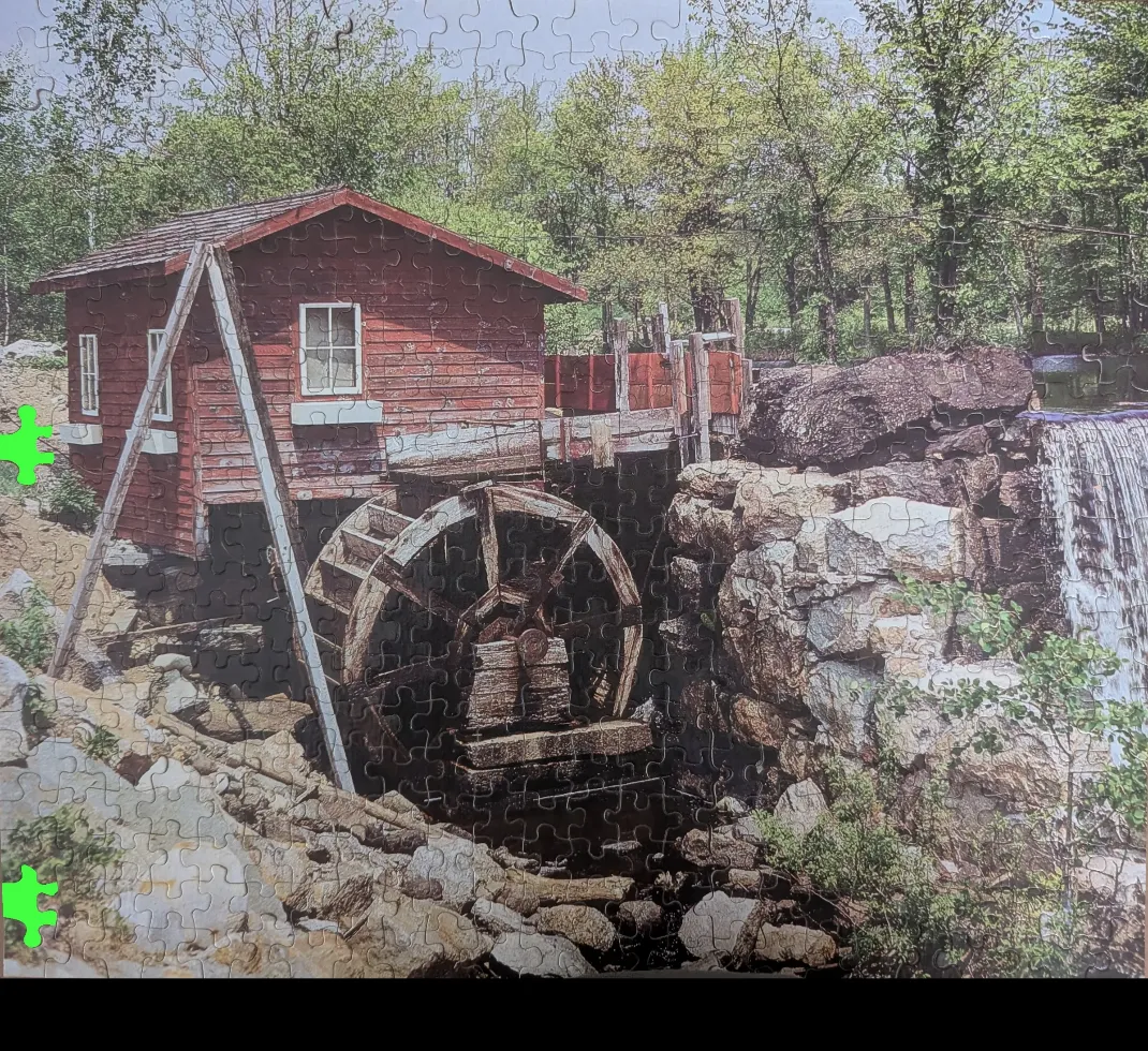 A rustic red wooden water mill sits beside a stone waterfall surrounded by lush green forest.