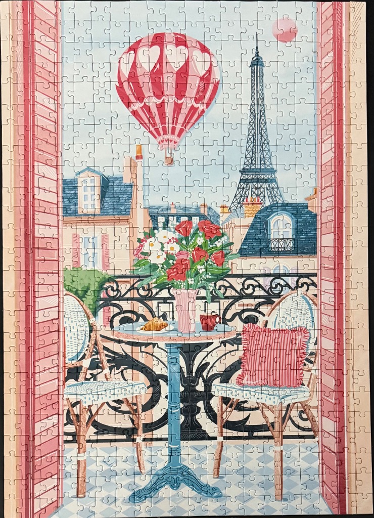 A view from a Parisian balcony with a hot air balloon, the Eiffel Tower, and a table set for breakfast.
