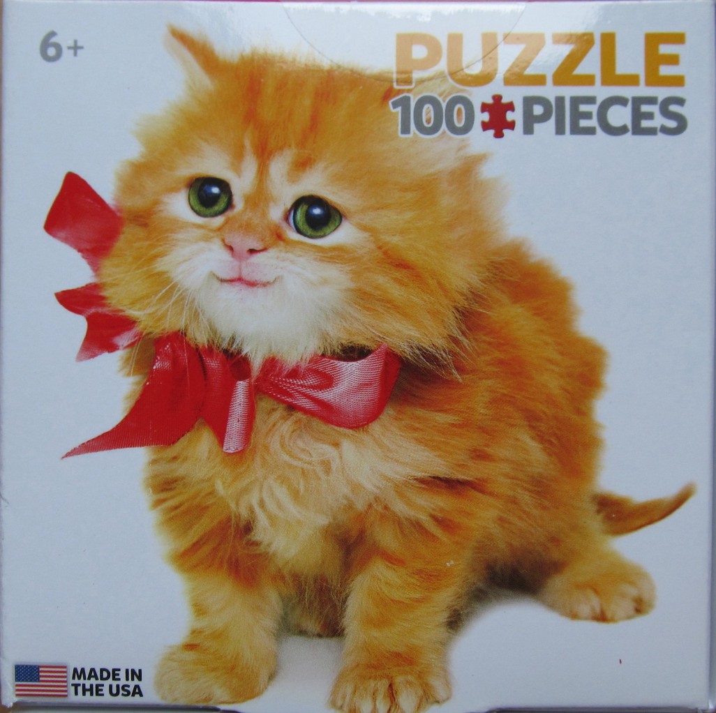 A fluffy ginger kitten with large green eyes and a bright red bow around its neck.